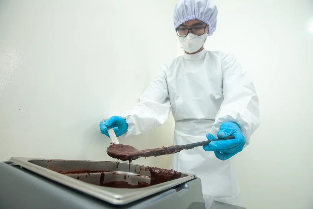 Cokelat yang sudah ditemper diangkat dengan sudip dari mesin temper